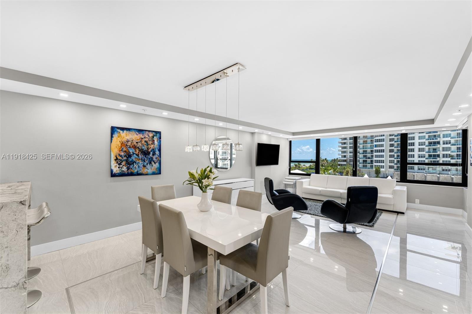 A modern dining and living area features white tile floors, a glass table, and ocean views — 5225 Collins Ave # 603, Miami Beach FL 33140, MIAMI BEACH, FL