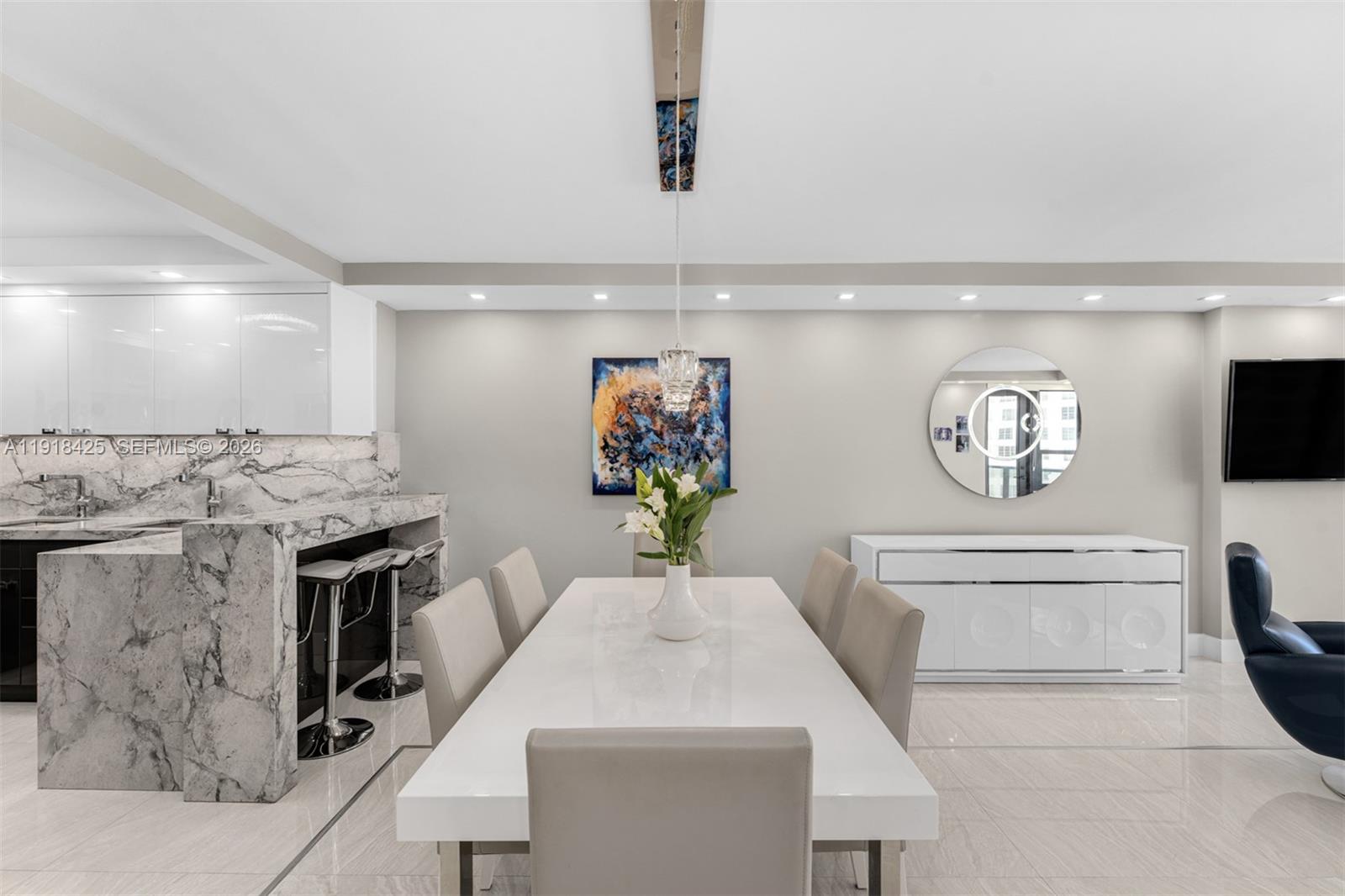 A dining room features a white table, six chairs, marble breakfast bar, and circular mirror — 5225 Collins Ave # 603, Miami Beach FL 33140, MIAMI BEACH, FL
