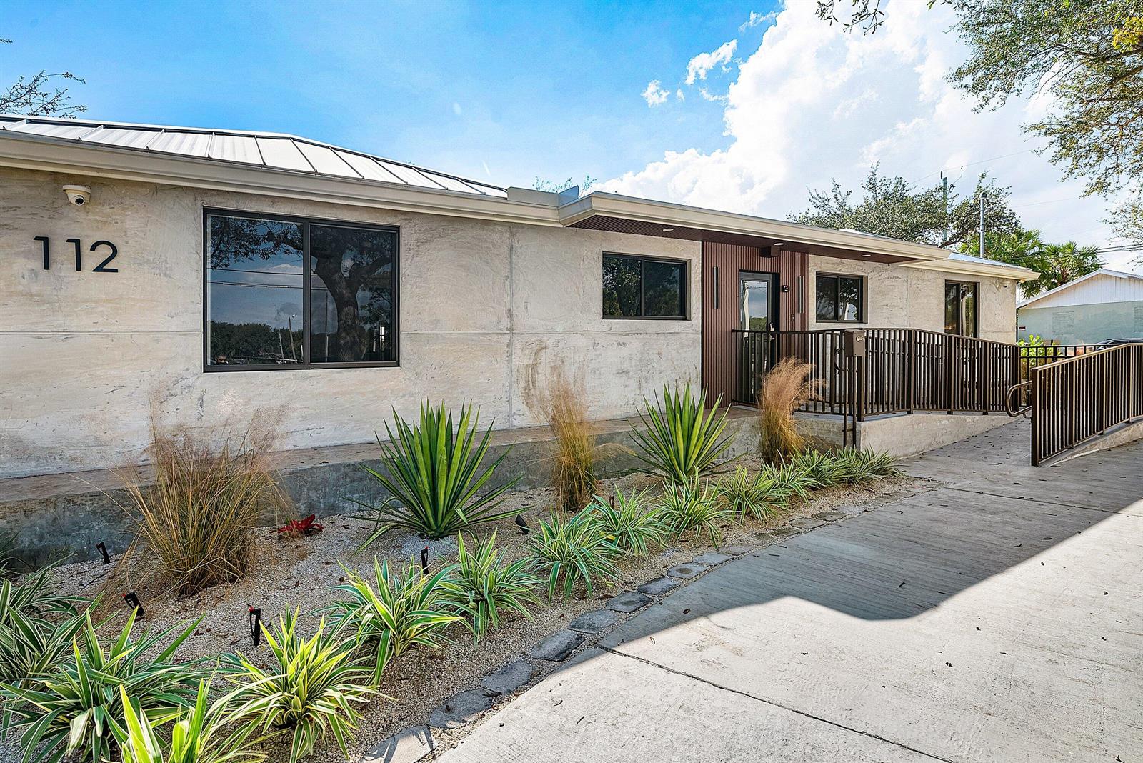 The exterior of a single-story building features light-colored concrete walls, a metal roof, and landscaping — 112 SE 10th Street, Delray Beach FL 33483, DELRAY BEACH, FL