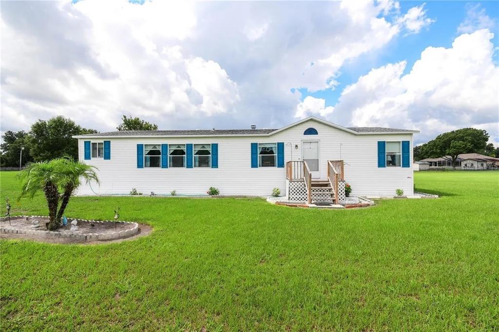 A single-story manufactured home with white siding and blue shutters sits on a grassy lot — 36630 CHANCEY ROAD, ZEPHYRHILLS, FL