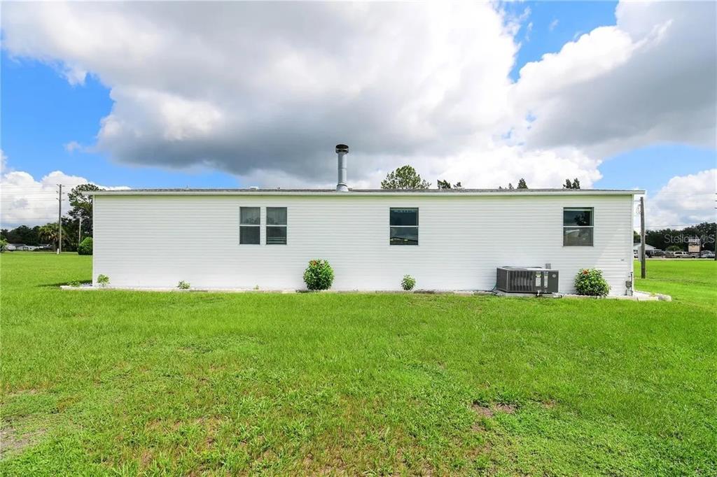 The exterior of a white single-story house with a metal chimney and green lawn — 36630 CHANCEY ROAD, ZEPHYRHILLS, FL