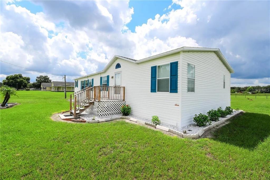 A white manufactured home with blue shutters sits on a grassy lot under a cloudy sky — 36630 CHANCEY ROAD, ZEPHYRHILLS, FL