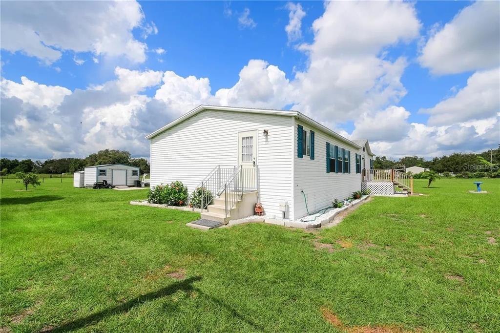 A white mobile home with blue shutters sits on a large, grassy lot — 36630 CHANCEY ROAD, ZEPHYRHILLS, FL