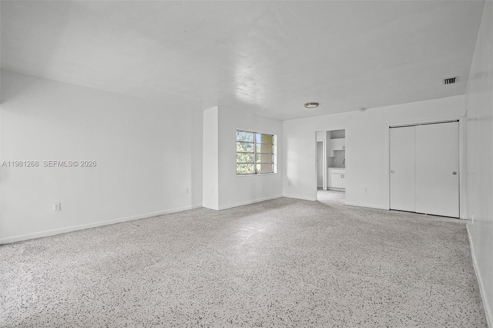 An empty room features white walls, gray speckled carpeting, a window, and a closet — 11330 Peachtree Dr, Miami FL 33161, MIAMI, FL
