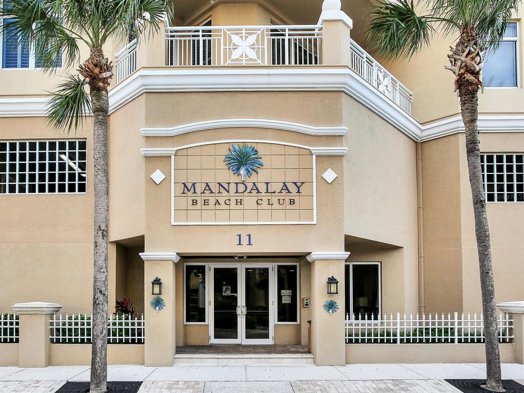The exterior entrance of the Mandalay Beach Club features palm trees and a glass door — 11 SAN MARCO STREET UNIT 807, CLEARWATER BEACH, FL