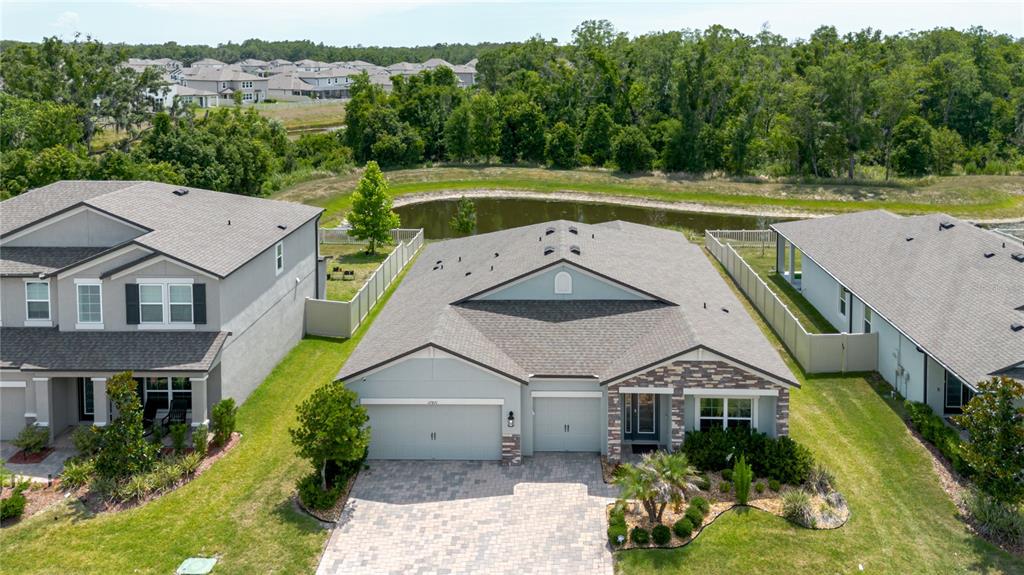An aerial view shows a single-story house with a paved driveway and a backyard pond — 17871 CORTES CREEK BOULEVARD, SPRING HILL, FL