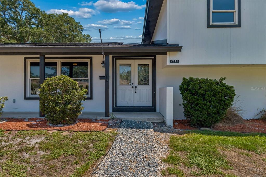 A white house exterior features a double front door, a gravel walkway, and two bushes — 7111 GATEWAY COURT, TAMPA, FL