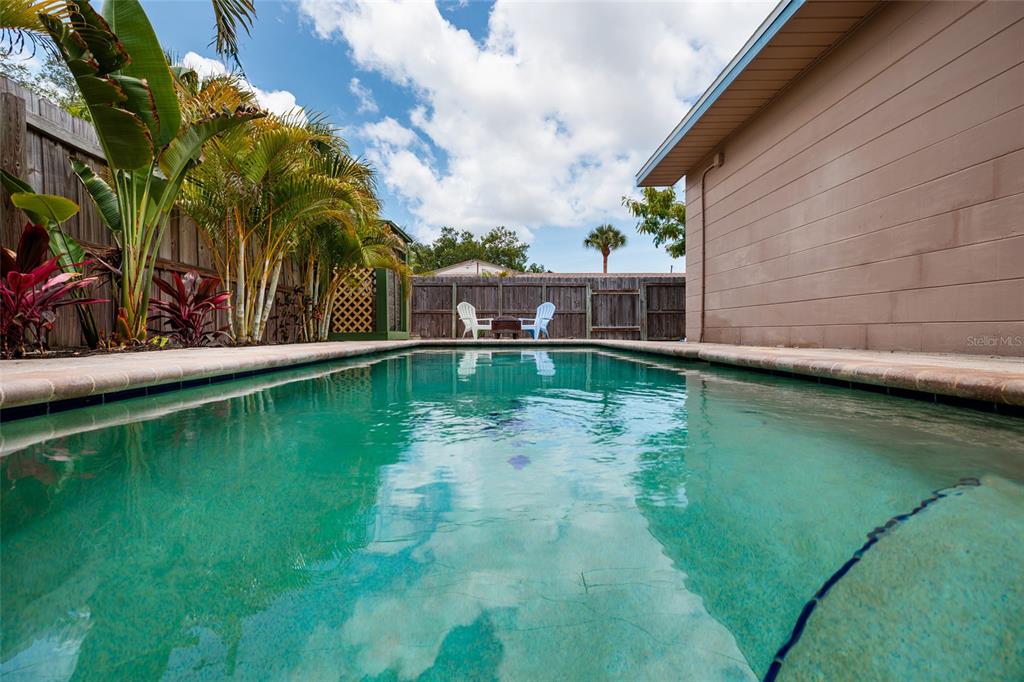 A swimming pool sits in a backyard with a wooden fence and two white chairs — 511 74TH AVENUE N, ST PETERSBURG, FL