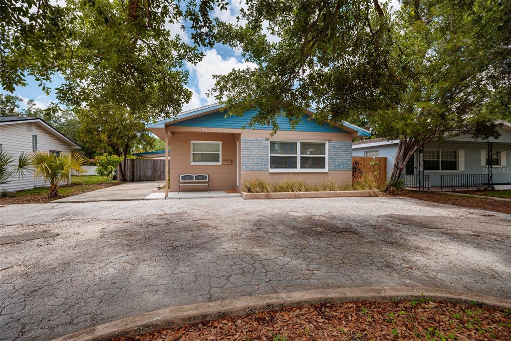 A single-story house with tan siding, blue accents, and a large cracked asphalt driveway — 511 74TH AVENUE N, ST PETERSBURG, FL