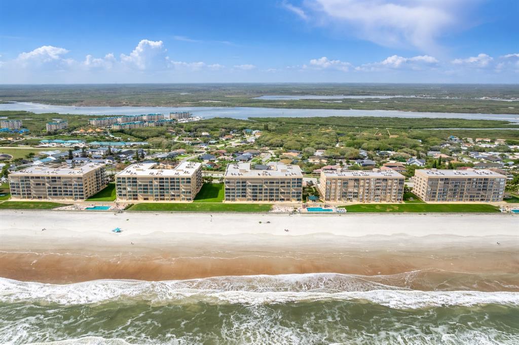 An aerial view shows five beachfront apartment buildings with swimming pools along a sandy shore — 4555 S ATLANTIC AVENUE UNIT 4506, PONCE INLET, FL