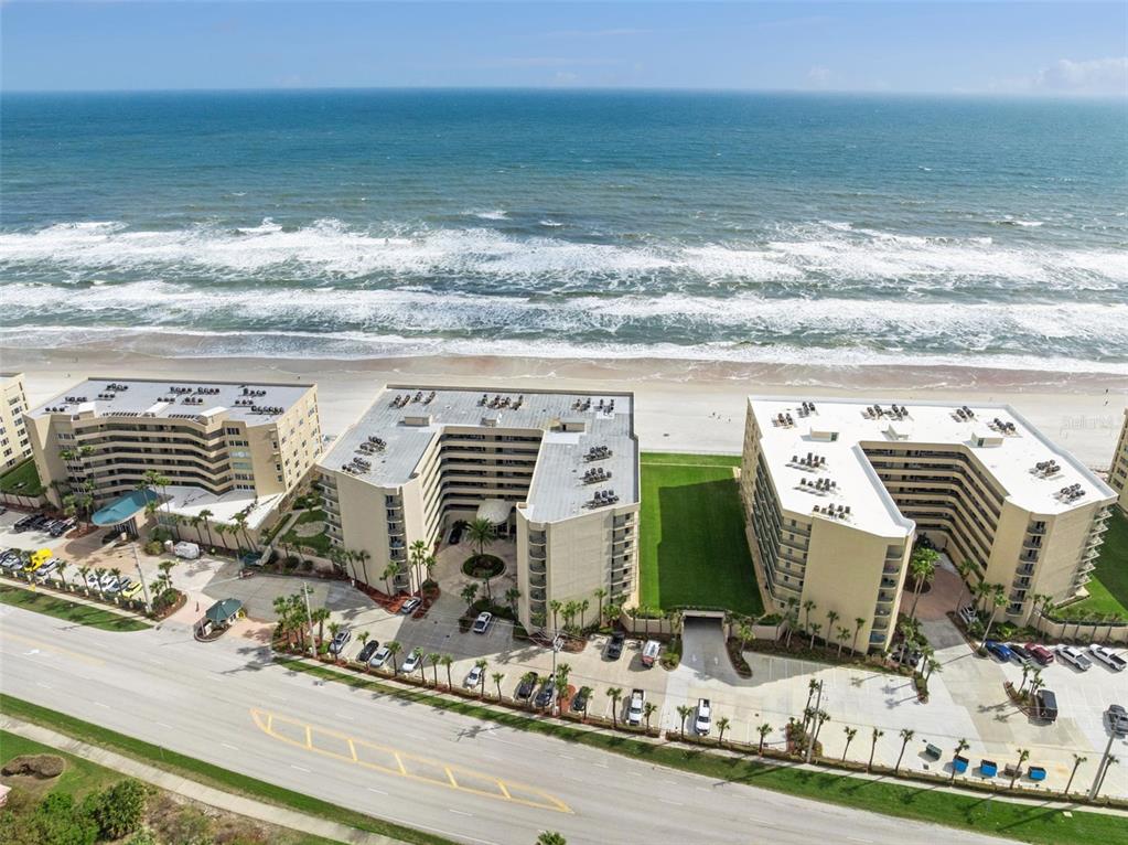 An aerial view shows three U-shaped beachfront apartment buildings with parking lots along a road — 4555 S ATLANTIC AVENUE UNIT 4506, PONCE INLET, FL