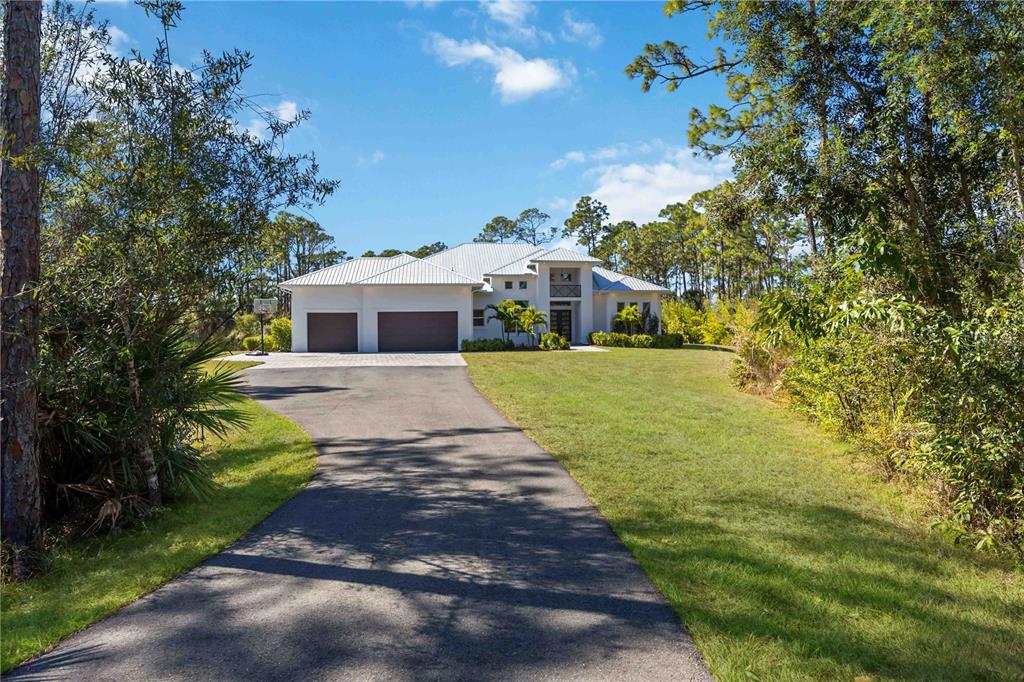A white single-story house with a metal roof and a two-car garage sits at the end of a long driveway — 143 CREEK DRIVE SE, PORT CHARLOTTE, FL