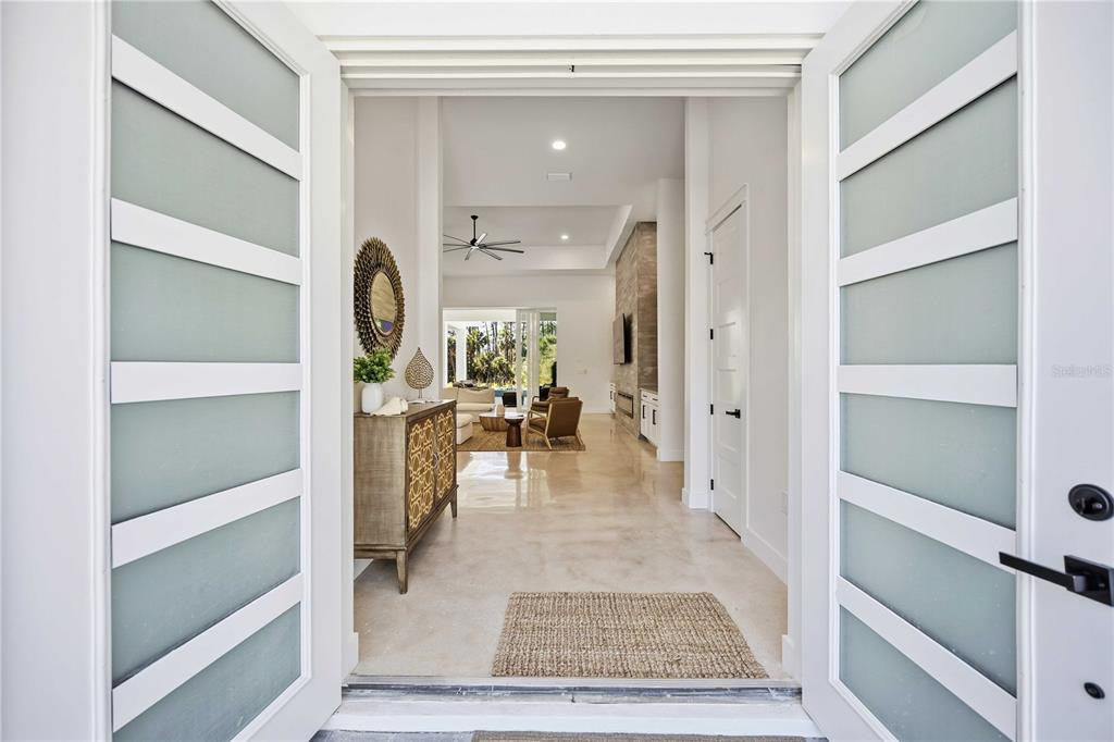 A view through open frosted glass double doors into a bright, modern home entryway — 143 CREEK DRIVE SE, PORT CHARLOTTE, FL