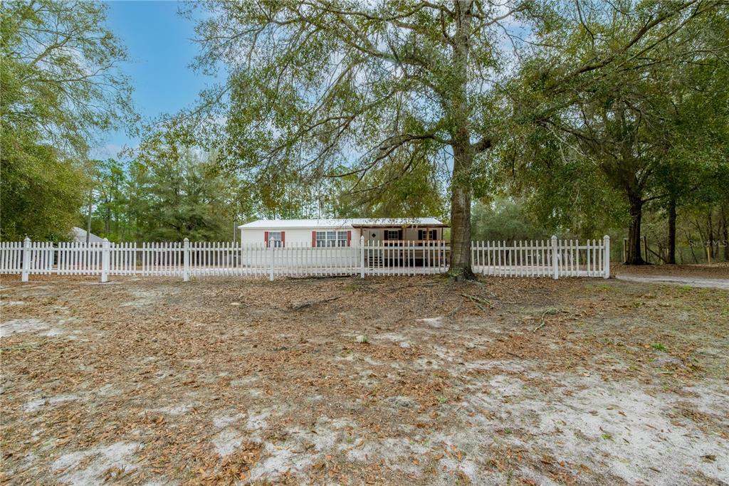 A white single-story house with red shutters sits behind a white picket fence — 5535 GILA STREET, KEYSTONE HEIGHTS, FL