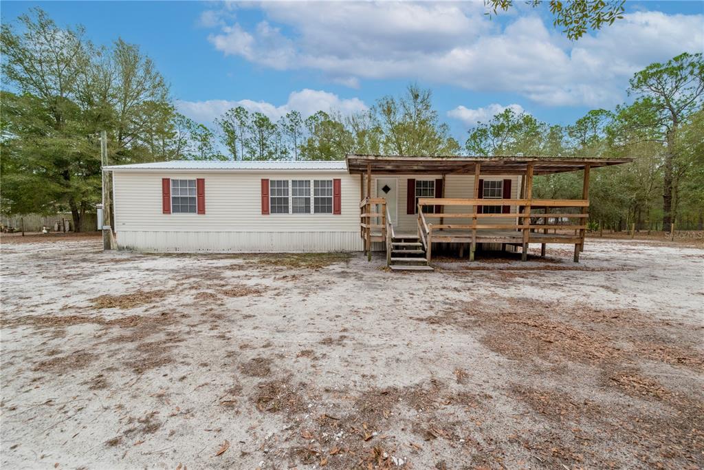 A single-story manufactured home with a wooden porch sits on a sandy, wooded lot — 5535 GILA STREET, KEYSTONE HEIGHTS, FL