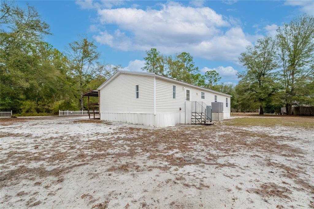 A side view of a light-colored mobile home with a metal staircase and sandy yard — 5535 GILA STREET, KEYSTONE HEIGHTS, FL