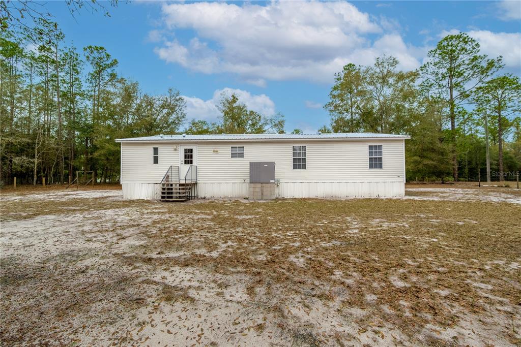 A single-story manufactured home with light siding stands on a sandy, wooded lot — 5535 GILA STREET, KEYSTONE HEIGHTS, FL