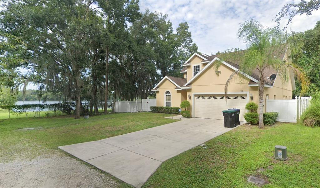 A two-story tan house with a concrete driveway and a white fence near a lake — 1518 SALEM DRIVE, ORLANDO, FL