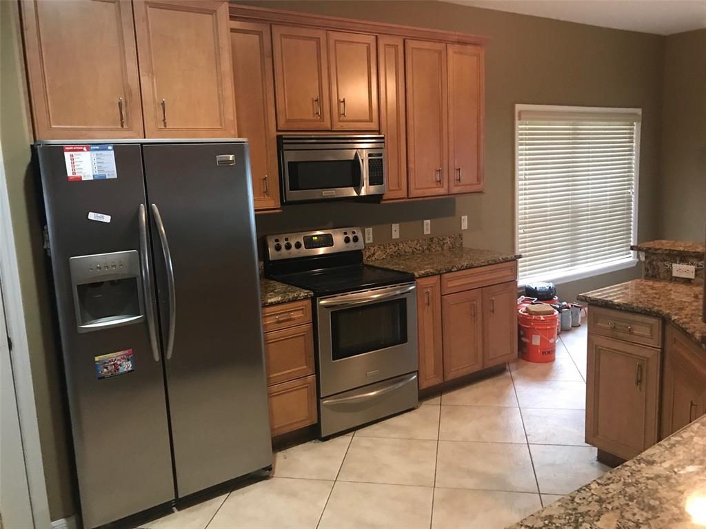 A kitchen features stainless steel appliances, wood cabinets, and granite countertops over tile flooring — 1518 SALEM DRIVE, ORLANDO, FL