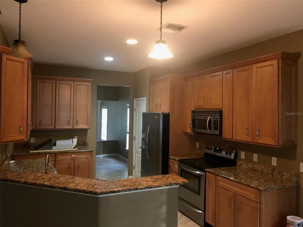 A kitchen features wood cabinets, granite countertops, stainless steel appliances, and two pendant lights — 1518 SALEM DRIVE, ORLANDO, FL