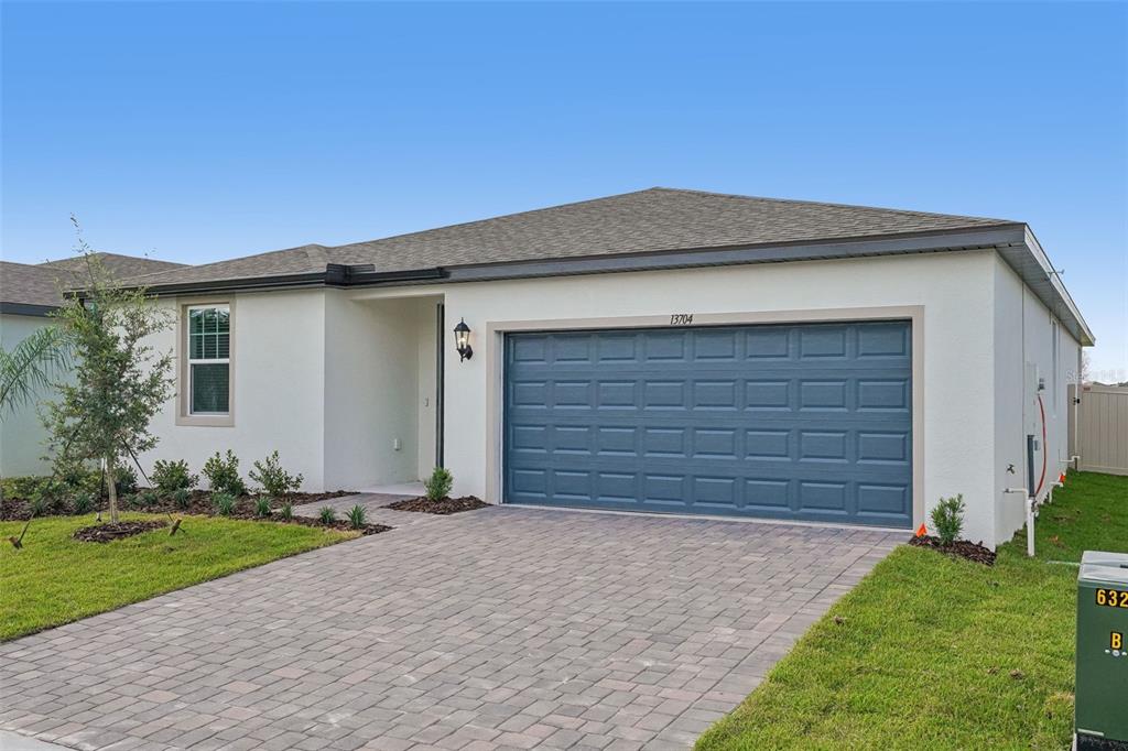 A single-story house with white stucco walls, a blue garage door, and a paver driveway — 13704 UMBER FOREST STREET, HUDSON, FL