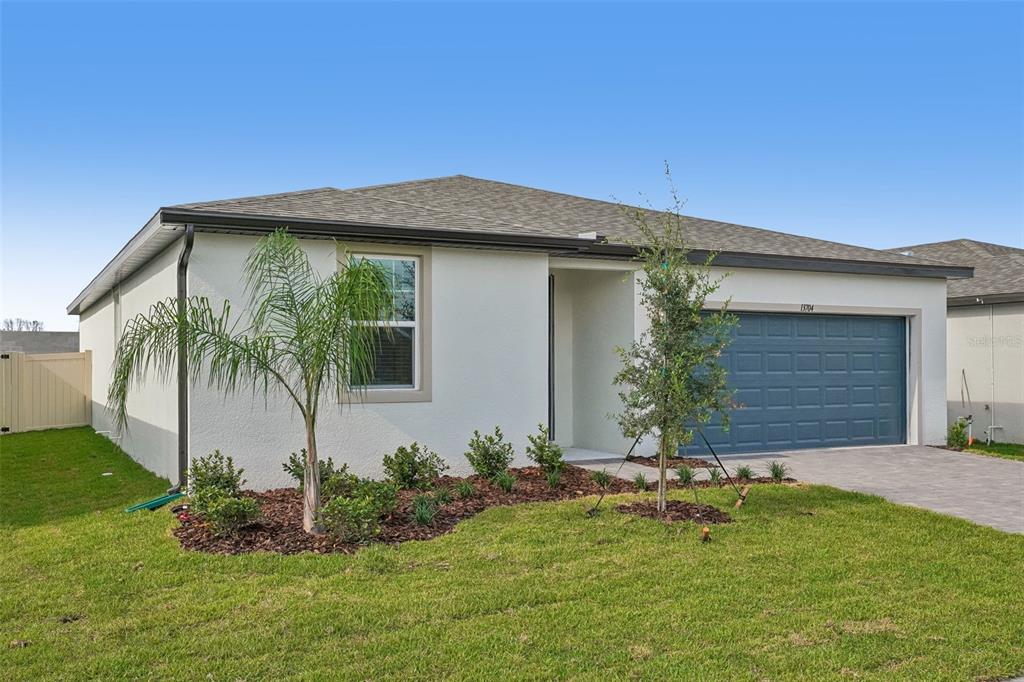 A single-story house with a white stucco exterior, a blue garage door, and a palm tree — 13704 UMBER FOREST STREET, HUDSON, FL
