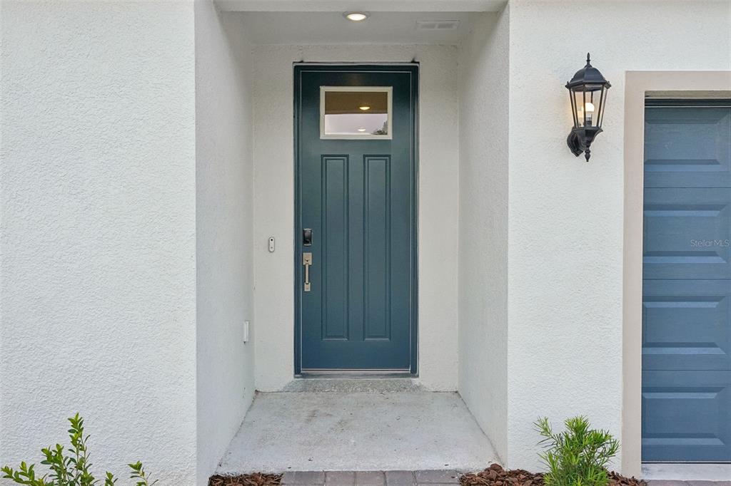 A teal front door with a small window sits in a recessed white stucco entryway — 13704 UMBER FOREST STREET, HUDSON, FL