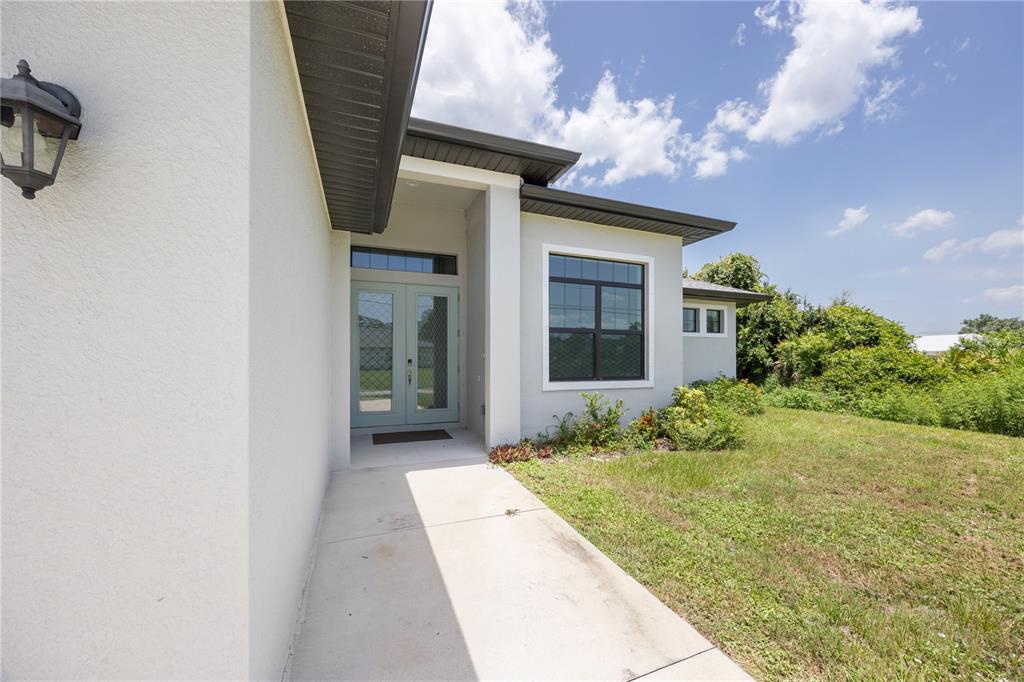 A concrete walkway leads to the double front doors of a light-colored stucco house — 2535 TRICO ROAD, NORTH PORT, FL