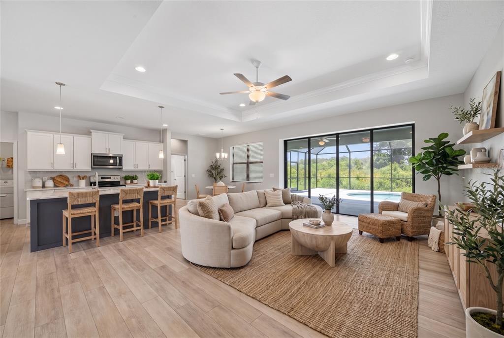 An open-concept living room and kitchen with a curved sofa, island seating, and pool view — 2535 TRICO ROAD, NORTH PORT, FL