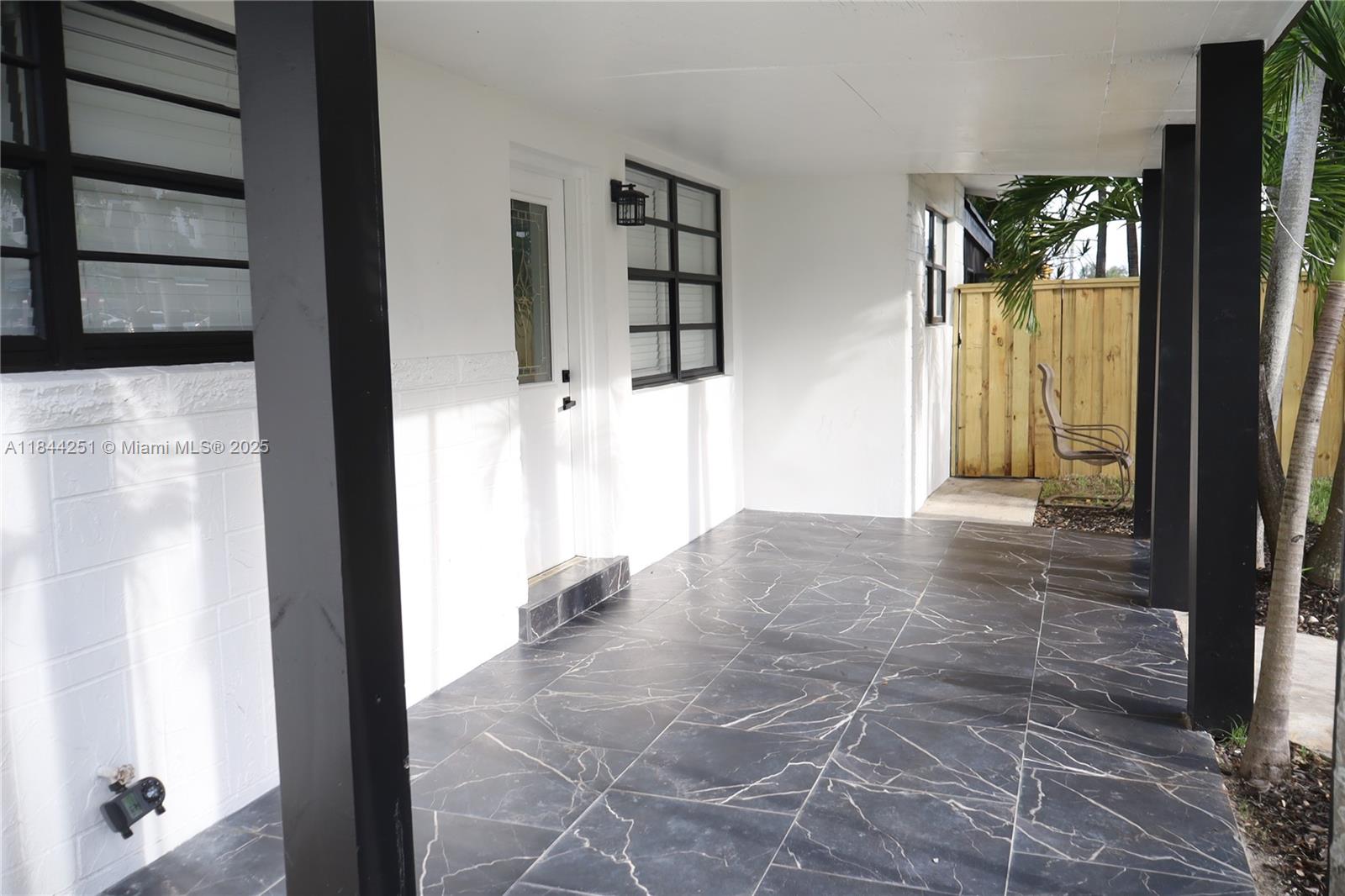 A covered porch features dark marble-patterned tile flooring, white exterior walls, and black support columns — 3955 SW 69th Ave, Miami FL 33155, MIAMI, FL