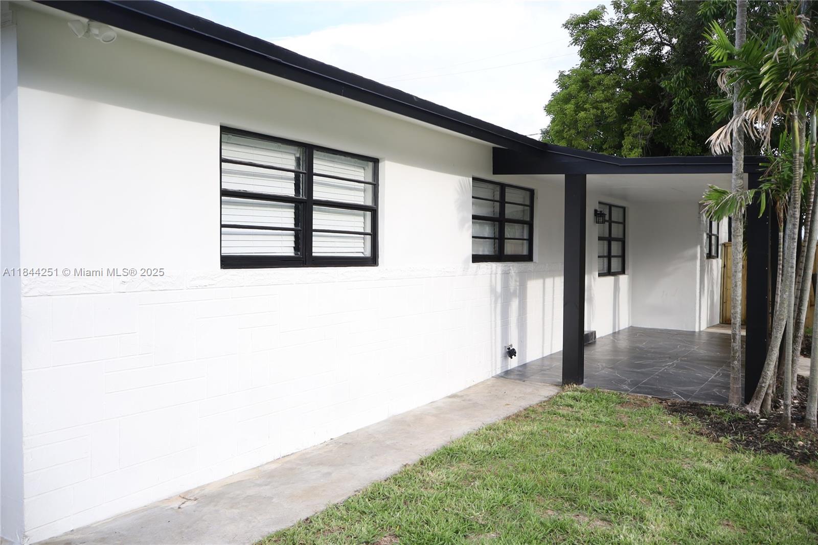 The exterior of a white house features black window frames, a covered patio, and landscaping — 3955 SW 69th Ave, Miami FL 33155, MIAMI, FL