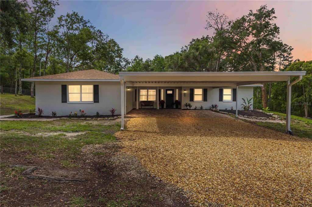 A single-story house with a gravel driveway, a large carport, and a light-colored exterior — 2293 SPRING LAKE HIGHWAY, BROOKSVILLE, FL