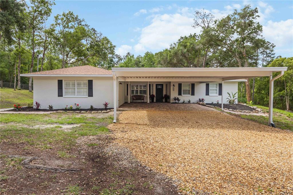 A single-story white house with a gravel driveway and a large attached carport — 2293 SPRING LAKE HIGHWAY, BROOKSVILLE, FL