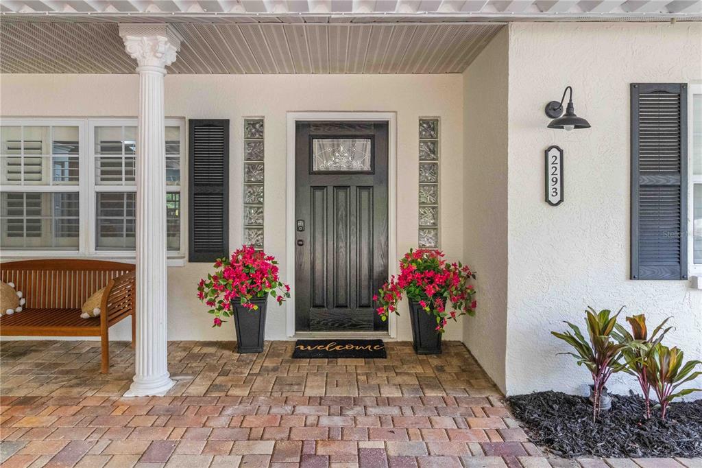 A front porch features a black door, two potted pink plants, and a wooden bench — 2293 SPRING LAKE HIGHWAY, BROOKSVILLE, FL