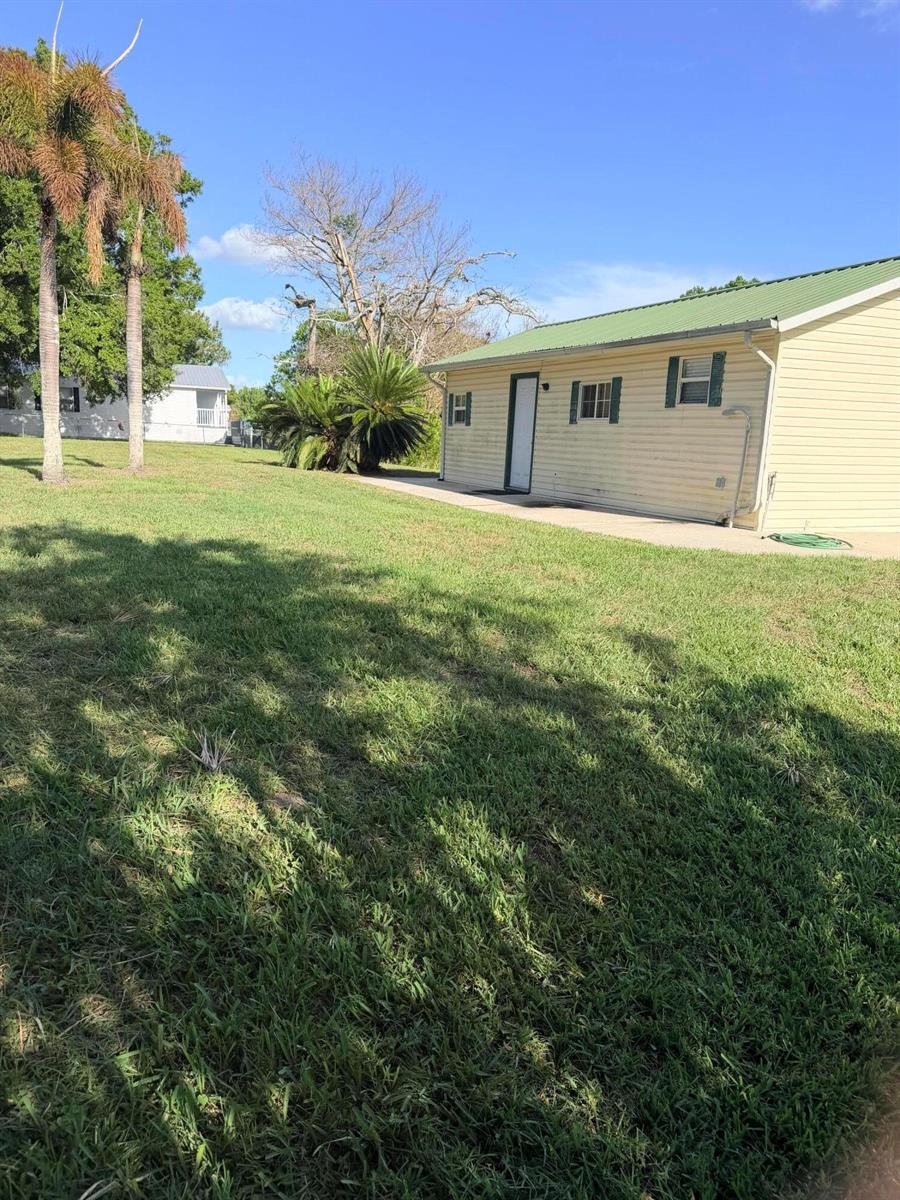 A side view of a yellow house with a green metal roof and lawn — 4046 SE 26th Street, Okeechobee FL 34974, OKEECHOBEE, FL