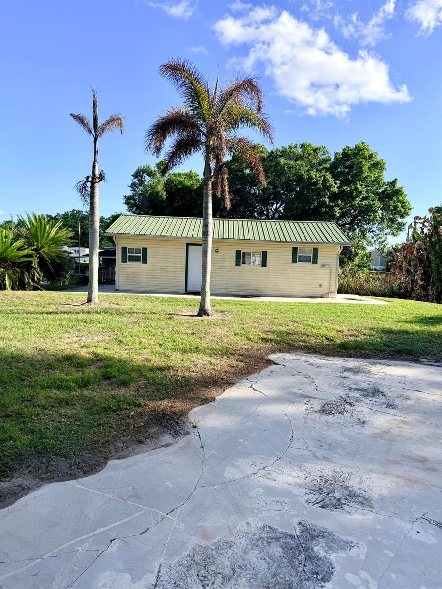 A light-colored, single-story building with a green metal roof stands behind two palm trees — 4046 SE 26th Street, Okeechobee FL 34974, OKEECHOBEE, FL