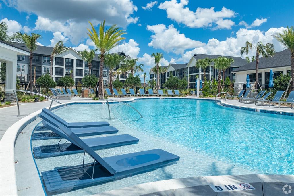 A swimming pool with submerged lounge chairs and surrounding apartment buildings under a blue sky — 3020 BASE BOULEVARD UNIT B2, DAVENPORT, FL
