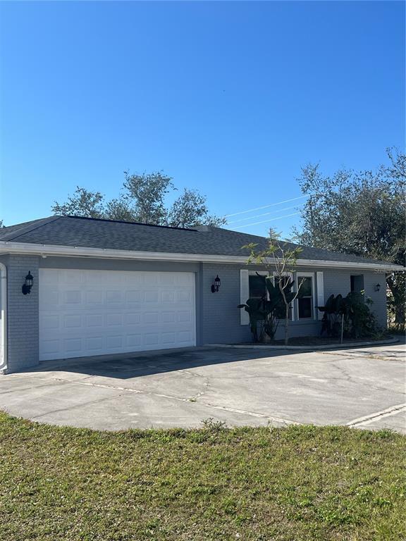 A gray brick house features a white garage door, dark roof, and a concrete driveway — 22065 MALONE AVENUE, PORT CHARLOTTE, FL