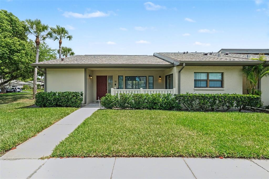 A single-story residential building with a tan stucco exterior, a red front door, and landscaping — 10 LESLEY LANE, OLDSMAR, FL