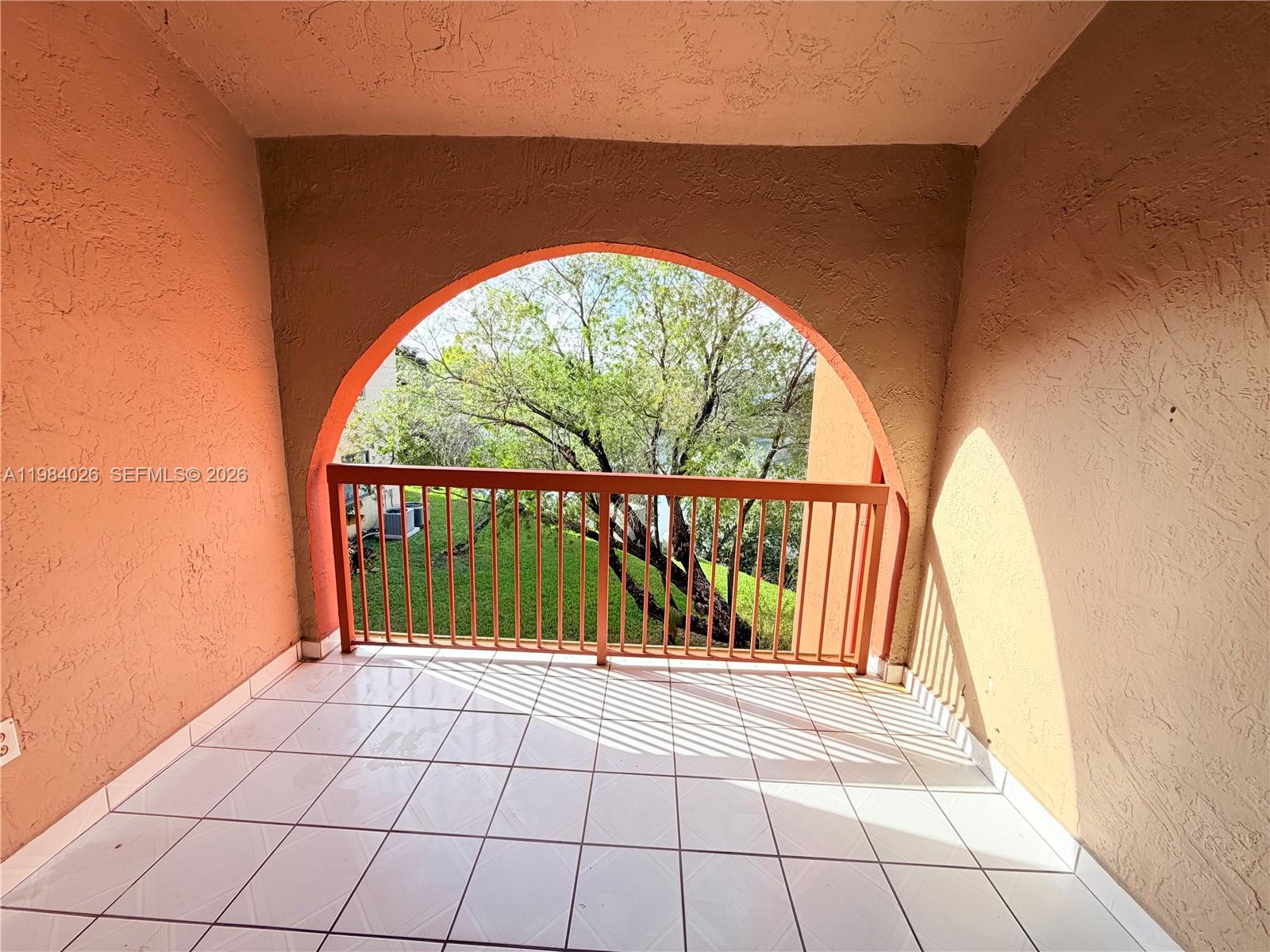 A covered balcony features white tiled flooring, peach-colored stucco walls, and an arched opening — 10233 NW 9 ST # 1, Miami FL 33172, MIAMI, FL