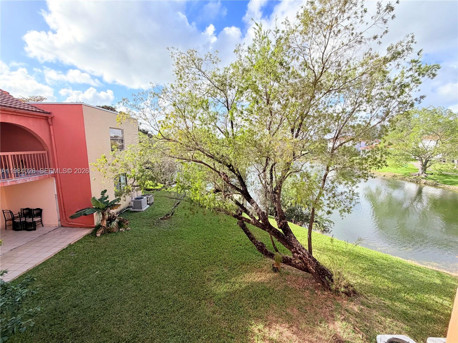 A view of a grassy backyard with a large tree beside a small lake — 10233 NW 9 ST # 1, Miami FL 33172, MIAMI, FL