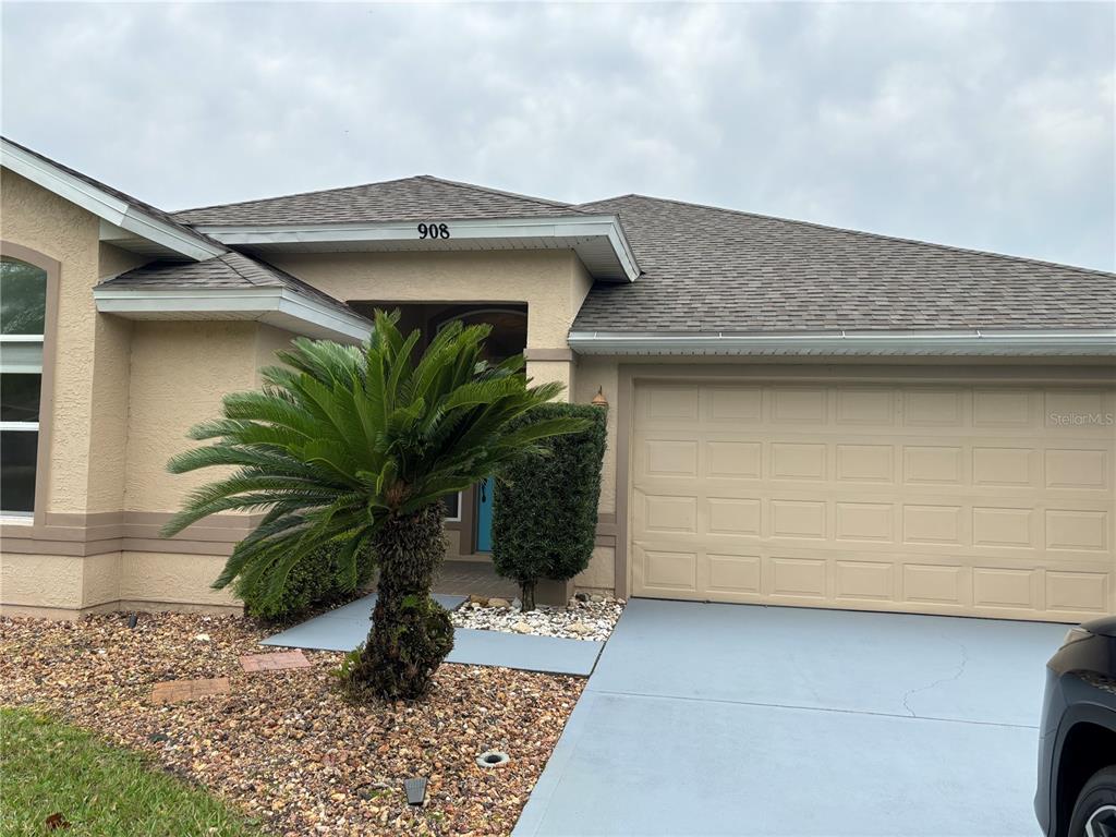 A single-story house exterior features a beige stucco facade, a two-car garage, and a palm tree — 908 WOODSTREAM LANE, ORMOND BEACH, FL