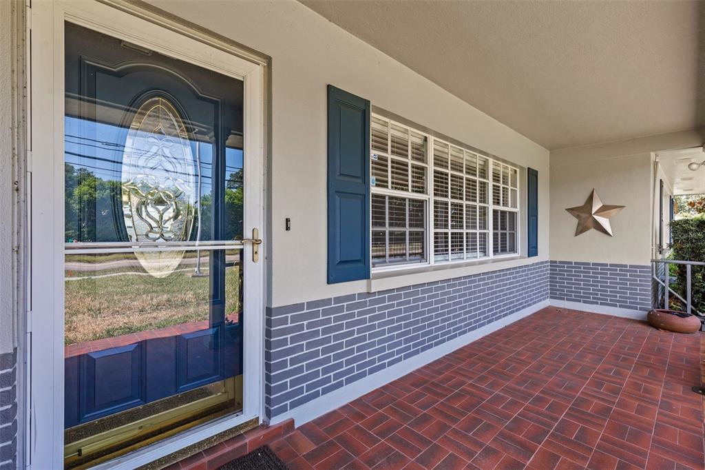 A covered front porch with red brick flooring, a blue storm door, and gray brick siding — 2087 DRUID ROAD E, CLEARWATER, FL