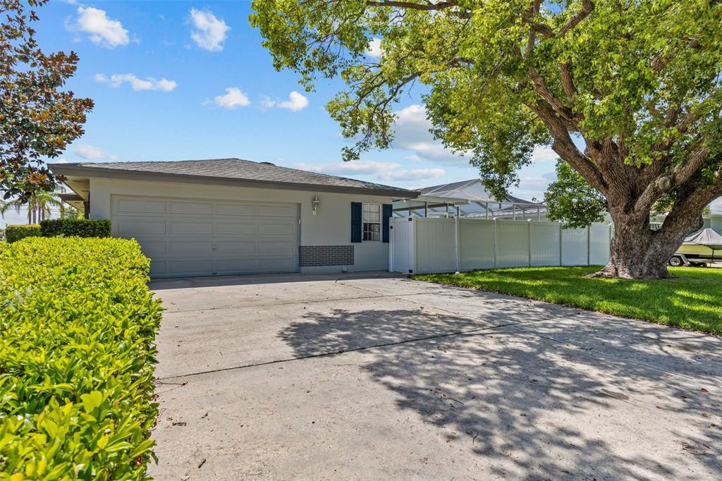 A single-story house with a gray garage, white vinyl fence, and a large oak tree — 2087 DRUID ROAD E, CLEARWATER, FL