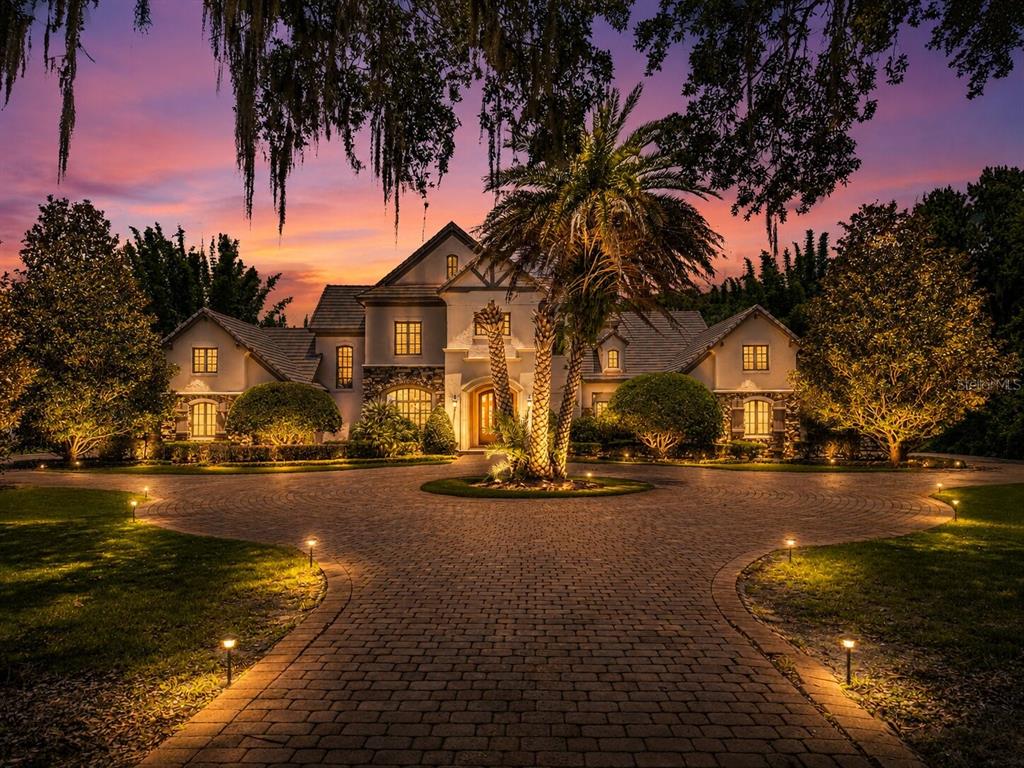 A large luxury home with a circular brick driveway at sunset, framed by Spanish moss — 680 LAKE MILLS ROAD, OVIEDO, FL