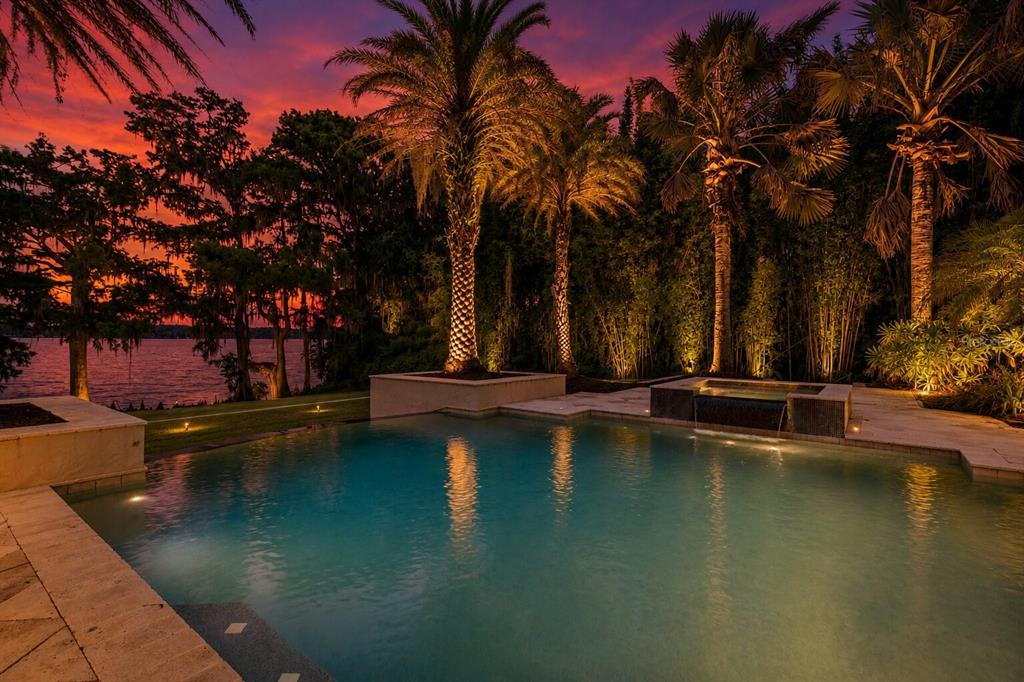 An illuminated swimming pool and hot tub overlook a lake at sunset with palm trees — 680 LAKE MILLS ROAD, OVIEDO, FL