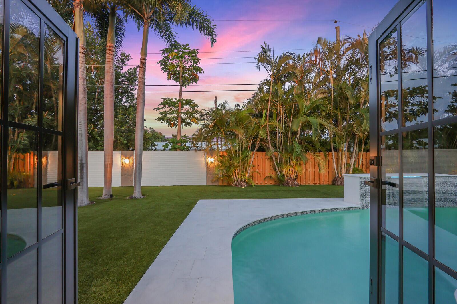 A view from an open doorway looking out at a backyard pool and palm trees — 391 W Riverside Drive, Tequesta FL 33469, TEQUESTA, FL