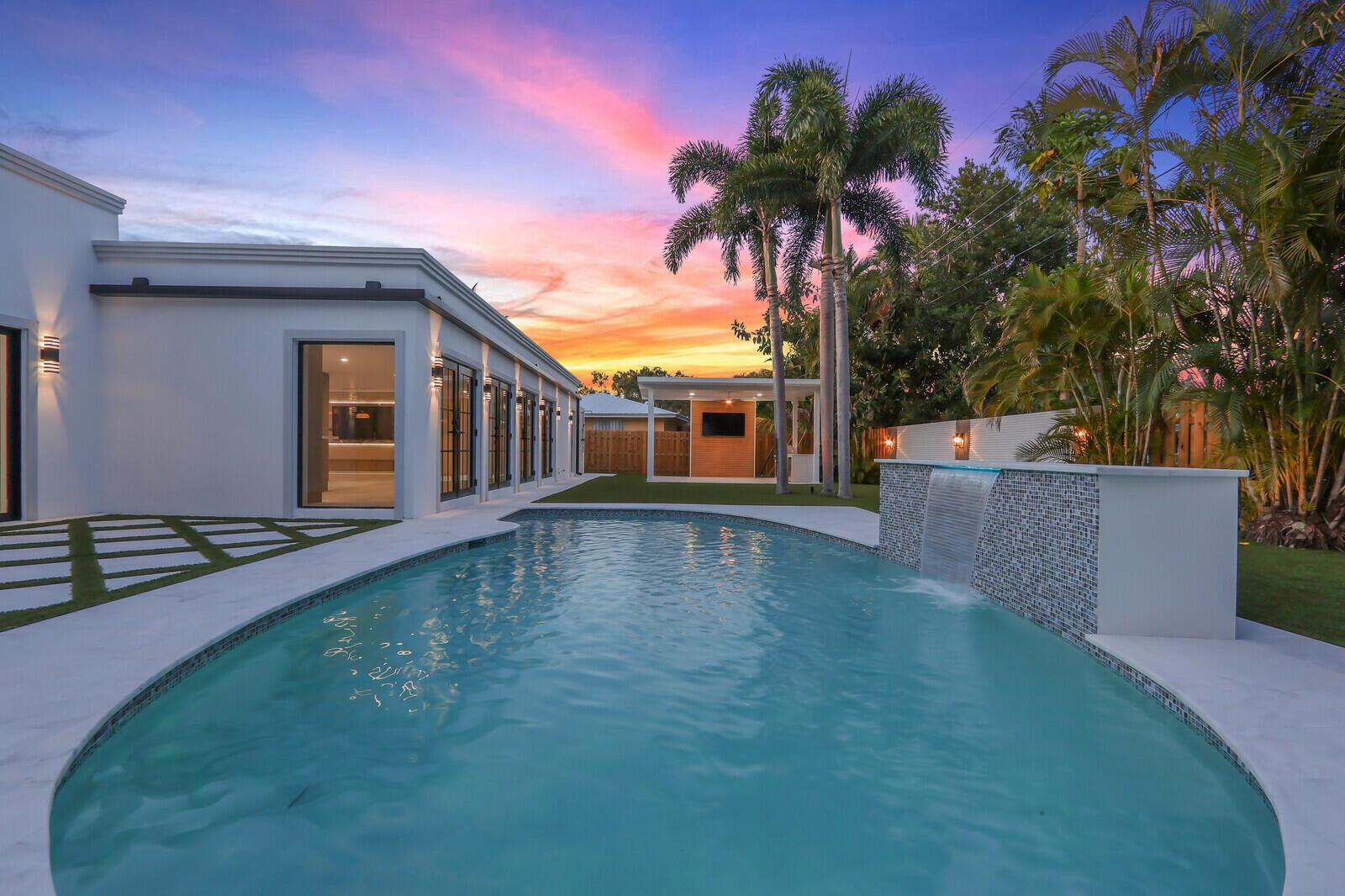 A modern white house with a pool, waterfall feature, and palm trees at sunset — 391 W Riverside Drive, Tequesta FL 33469, TEQUESTA, FL