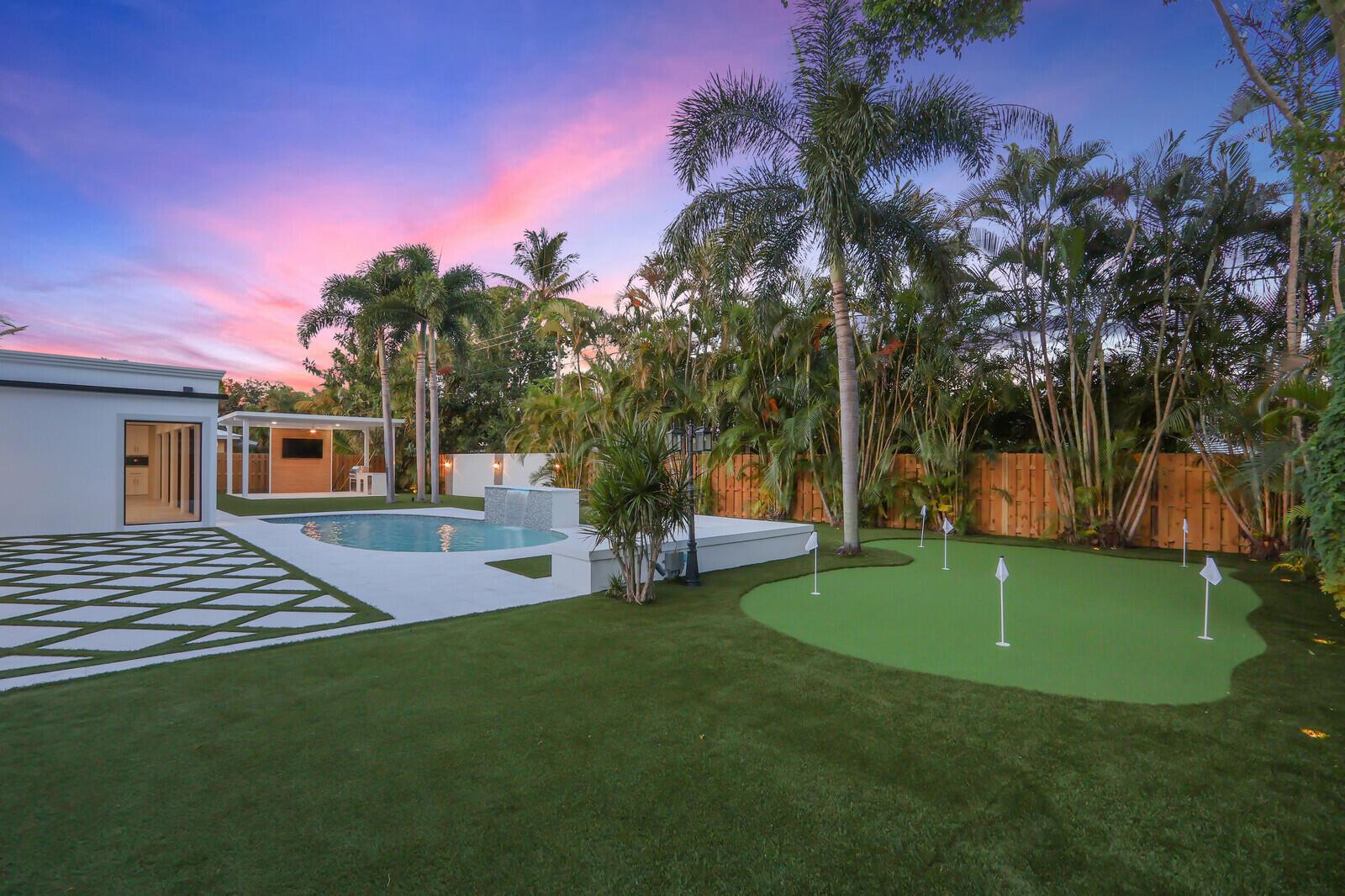 A backyard features a swimming pool, a putting green, and a patio at sunset — 391 W Riverside Drive, Tequesta FL 33469, TEQUESTA, FL