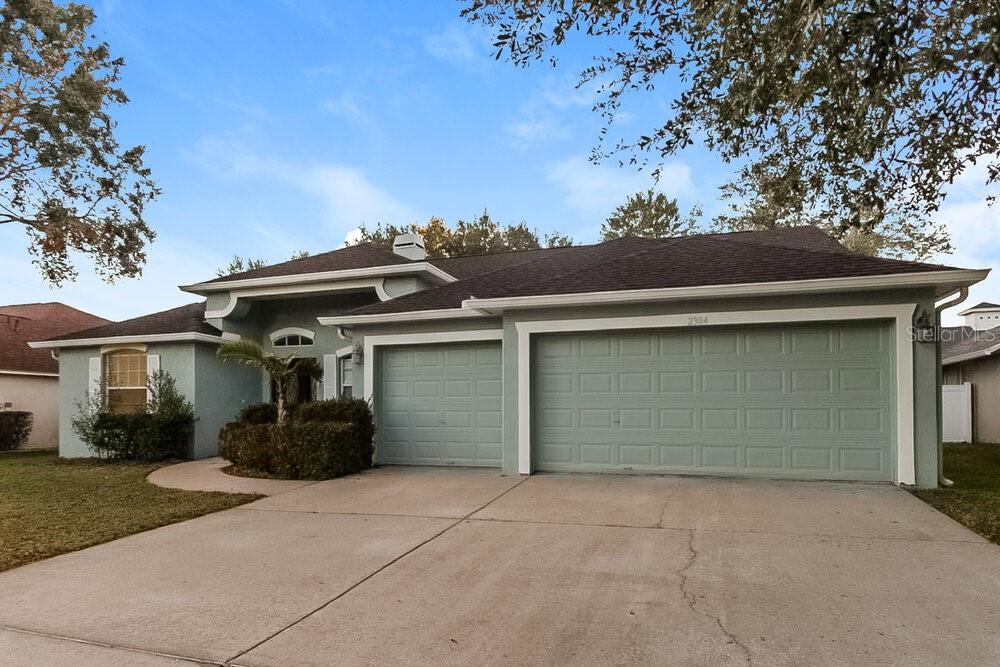 A light green single-story house features a three-car garage and a concrete driveway — 2304 GOLF MANOR BOULEVARD, VALRICO, FL